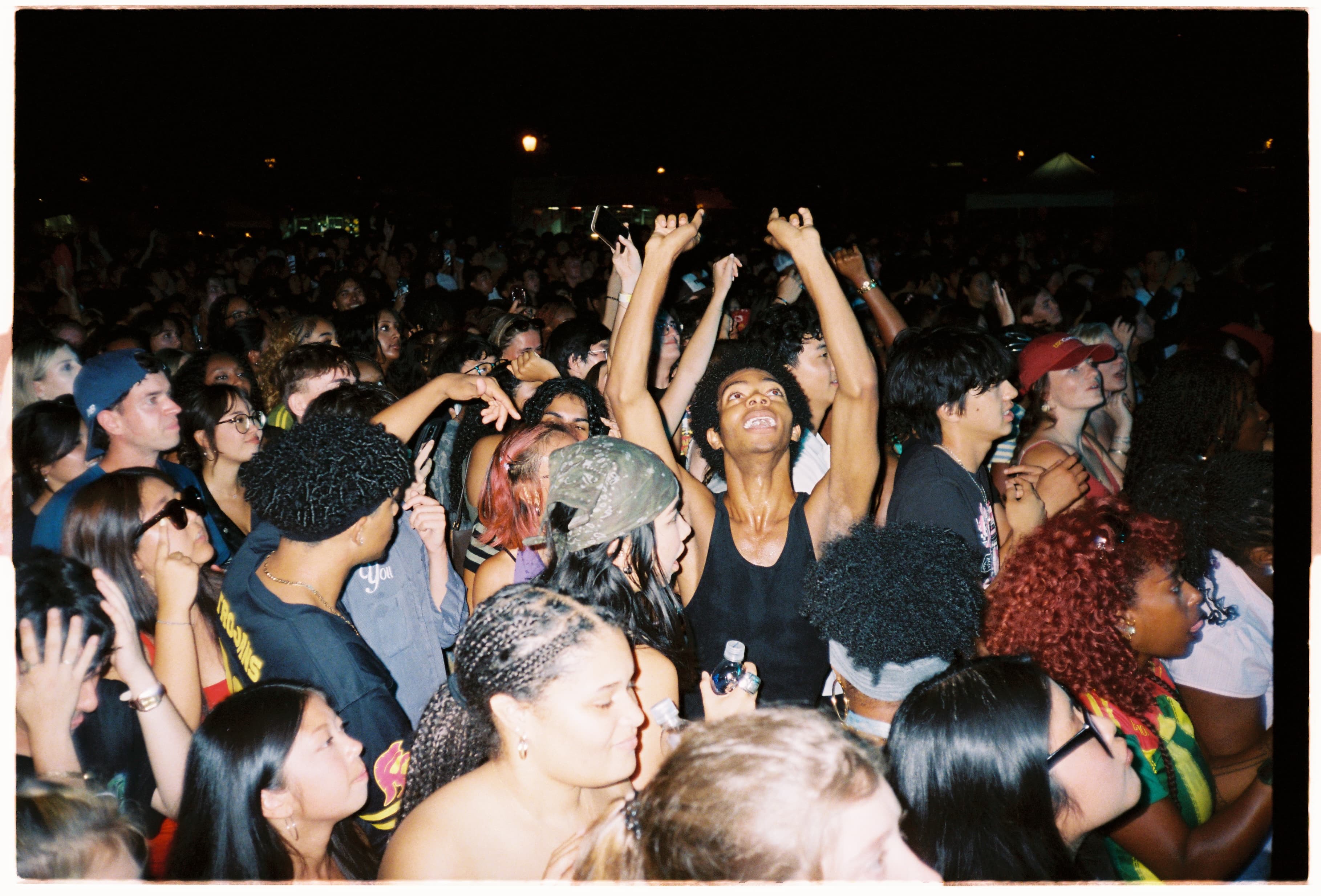 A packed crowd at night, one person cheering with both arms up.
